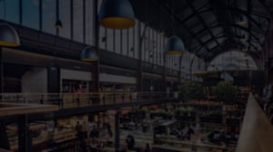 A bustling indoor market with lots of people walking between the stalls and goods, creating a lively atmosphere.